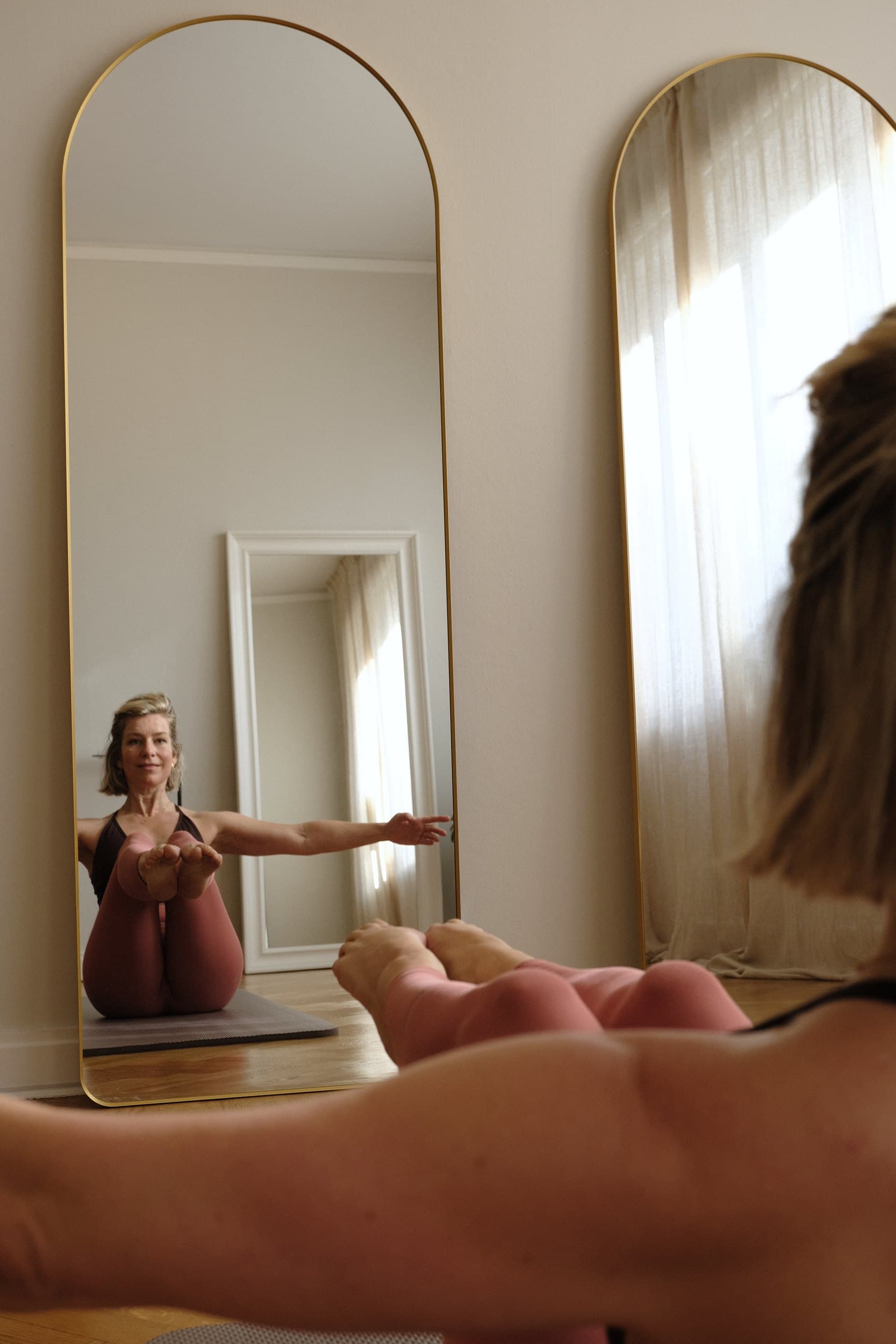 Liv balancing in a boat pose, seen in the studio's tall arched mirror.