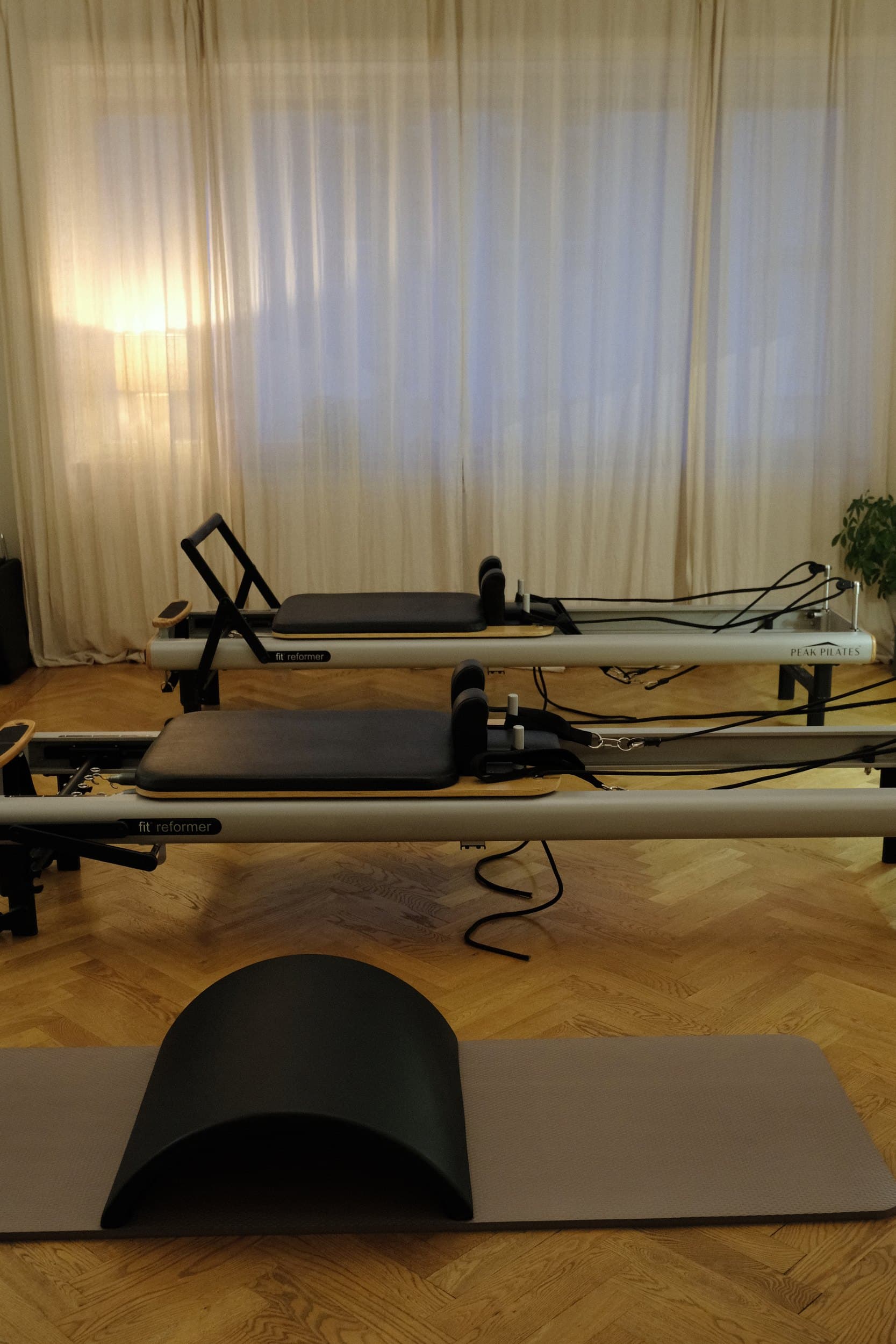 The home studio on Klostergatan: two Peak reformers, an arc barrel and a mat in warm light from curtained windows.